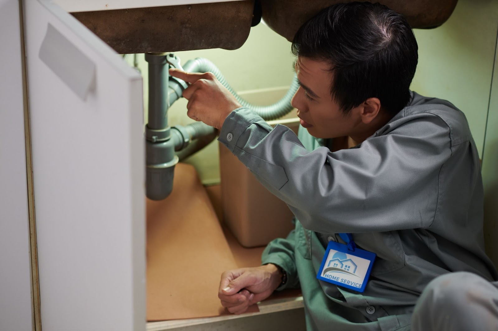 Plumbing service technician inspecting pipes under a kitchen sink.