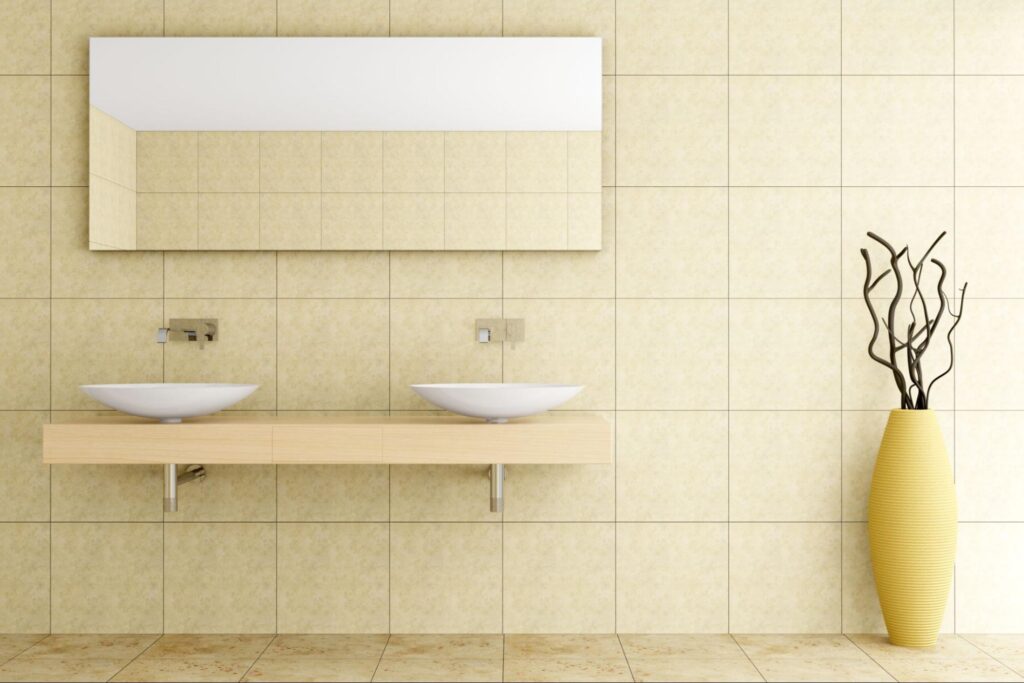 Modern bathroom with beige ceramic tiles on walls and floor, accented by a large yellow vase holding dried twigs.