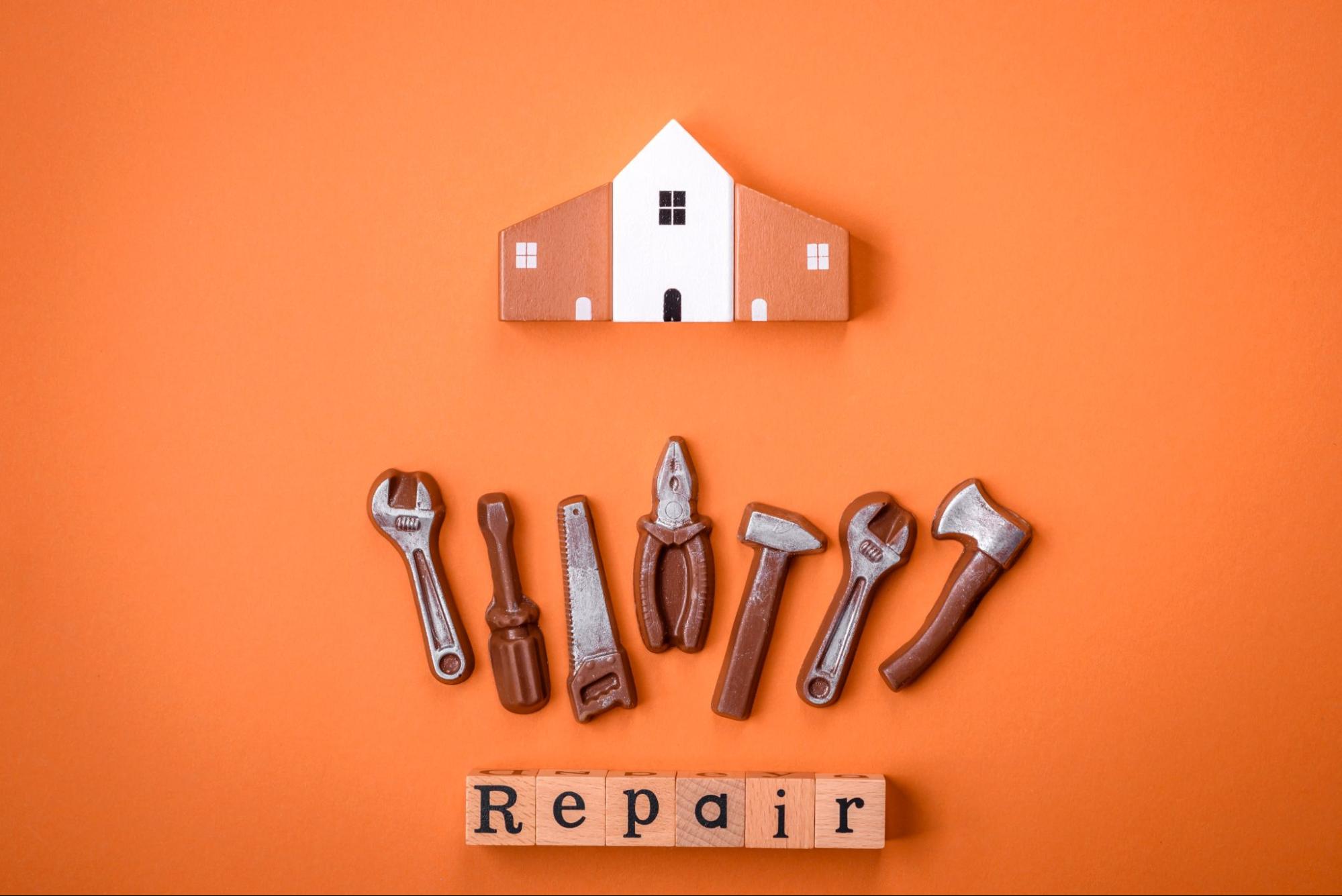 Symbolic home repair service setup with a model house and toy tools against a bright orange background.