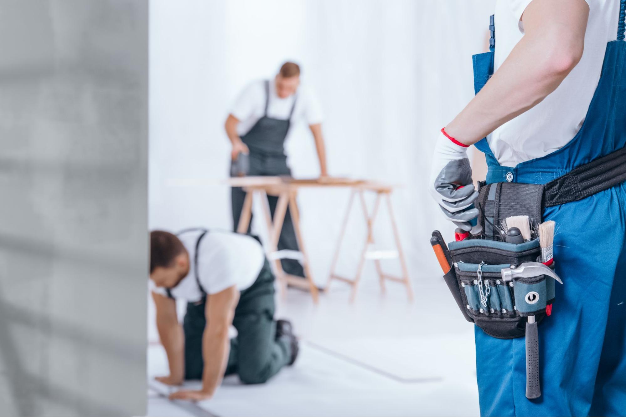 Home repair supervisor with a tool belt guiding two workers on-site.