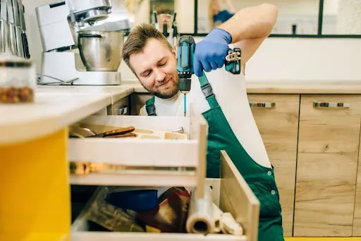 A local handyman fixing a kitchen drawer using a screw gun.