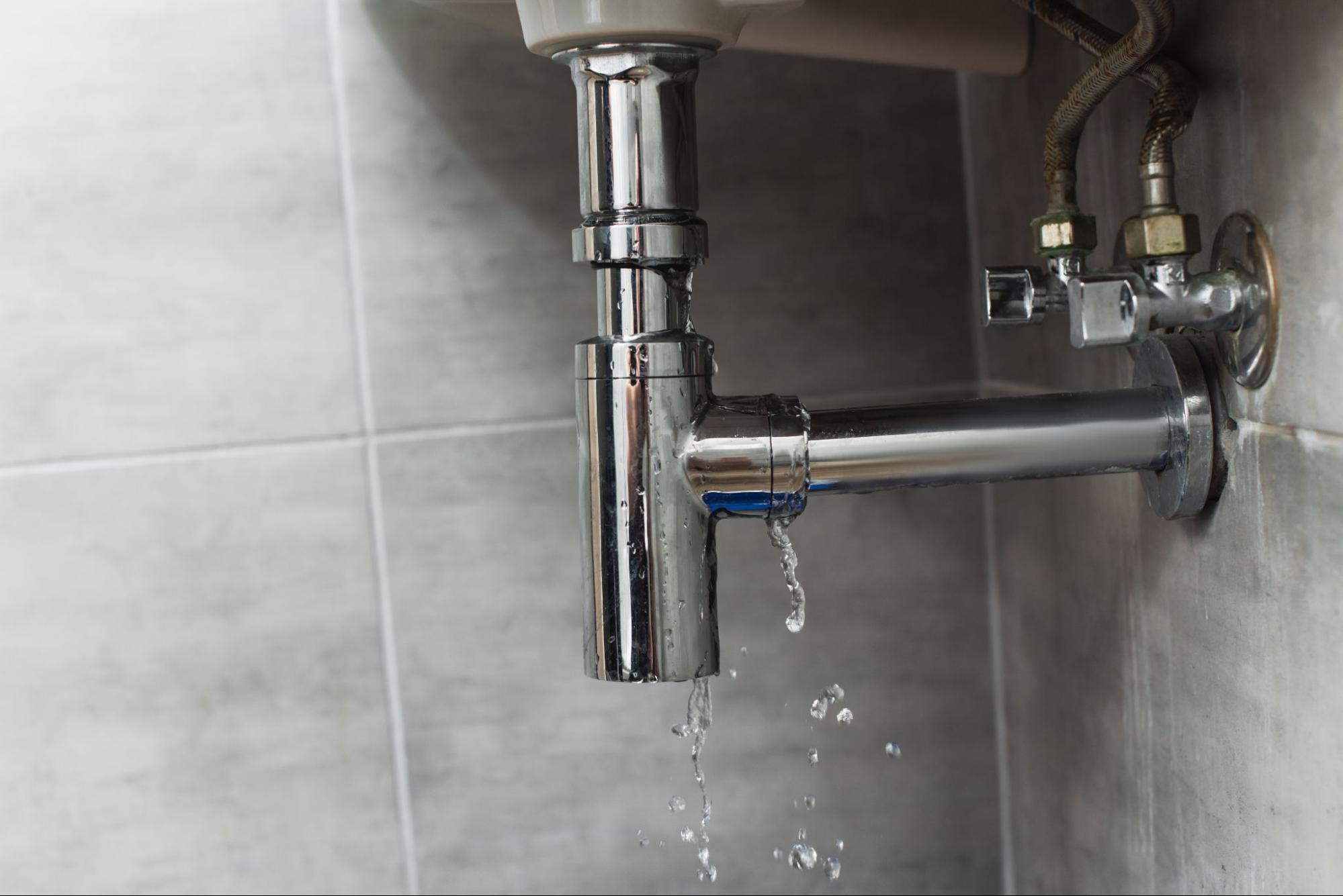 A corroded steel pipe under the sink against a gray wall background