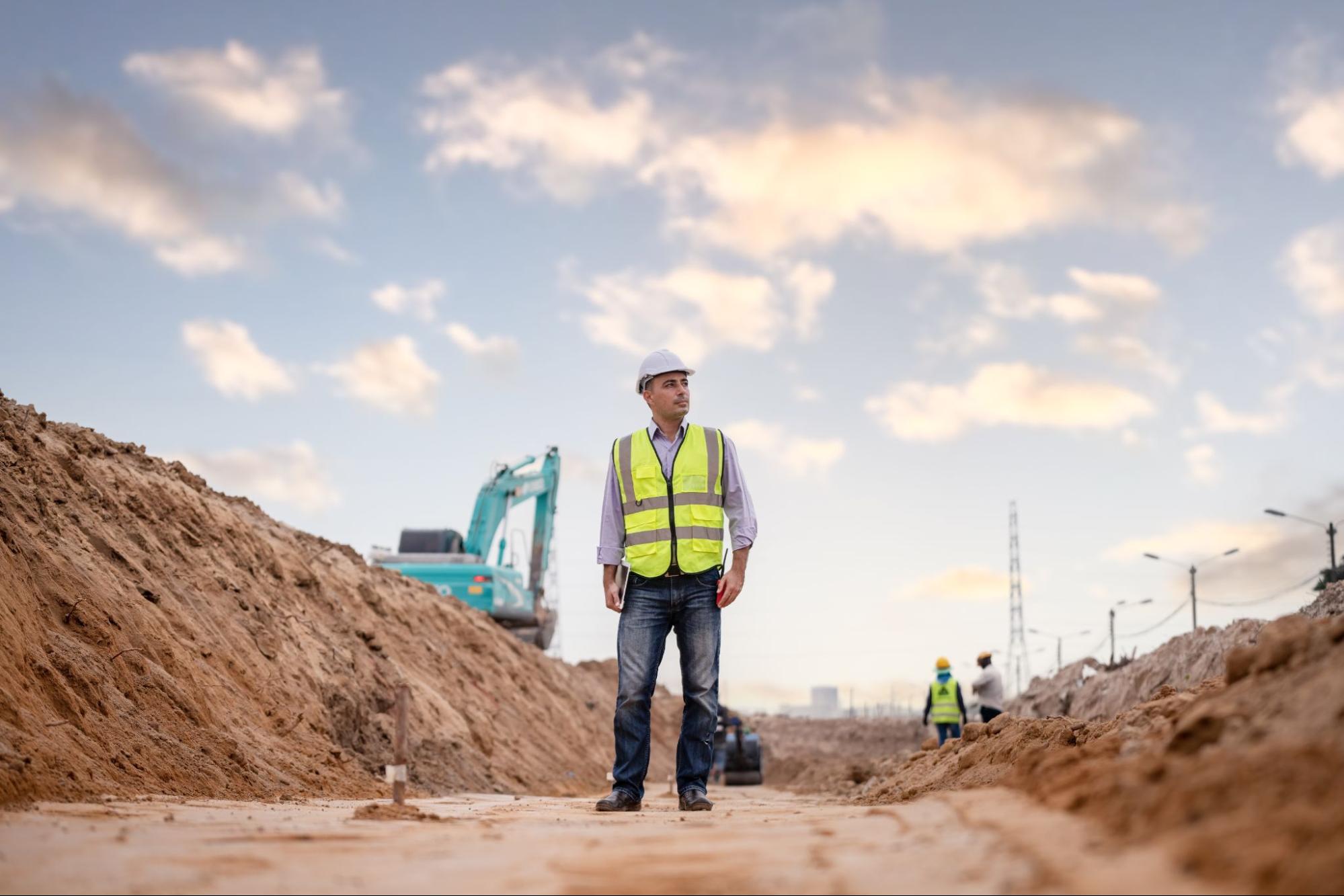 A professional contractor stands on a large outdoor job site in safety gear.
