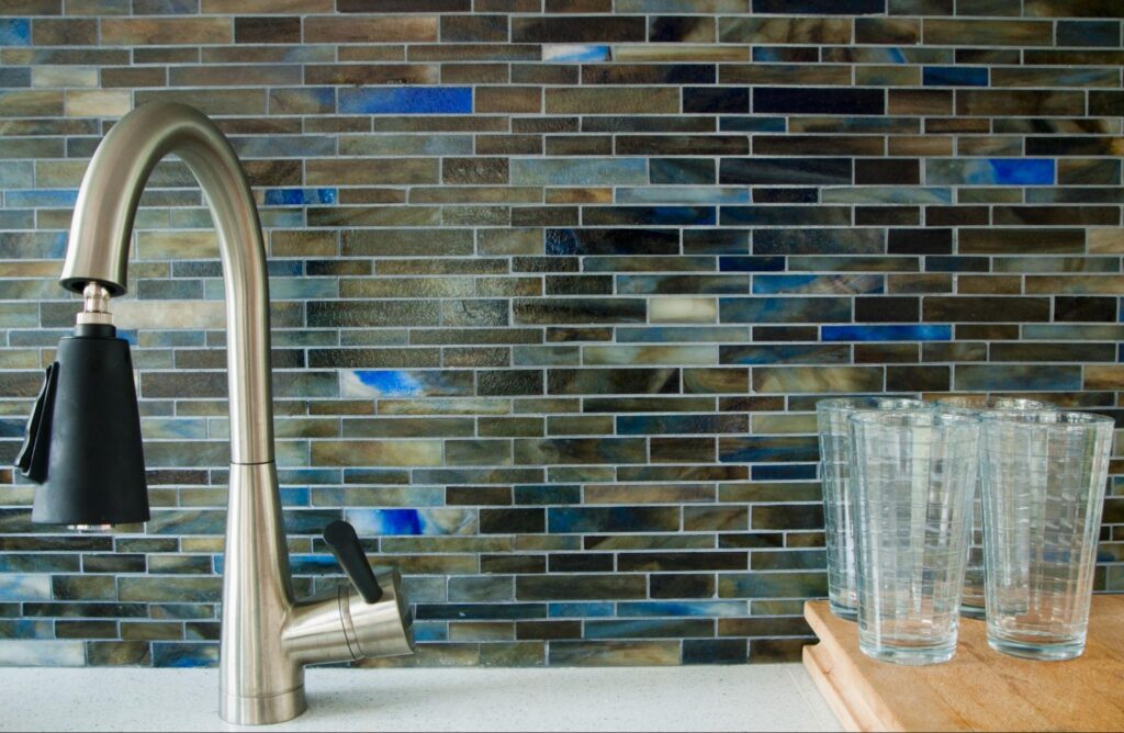 A modern kitchen faucet and blue, brown, and silver kitchen backsplash tile.