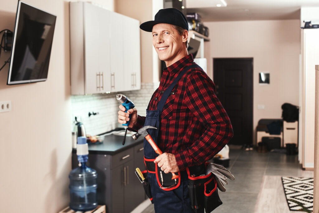 A smiling handyman services multiple projects in a kitchen.